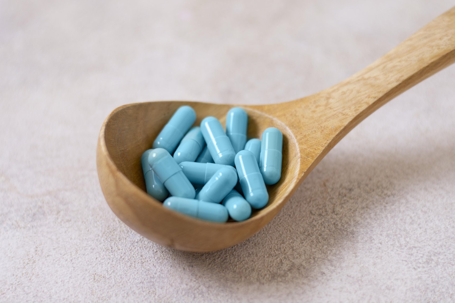 Top-down view of a wooden spoon filled with blue capsules.